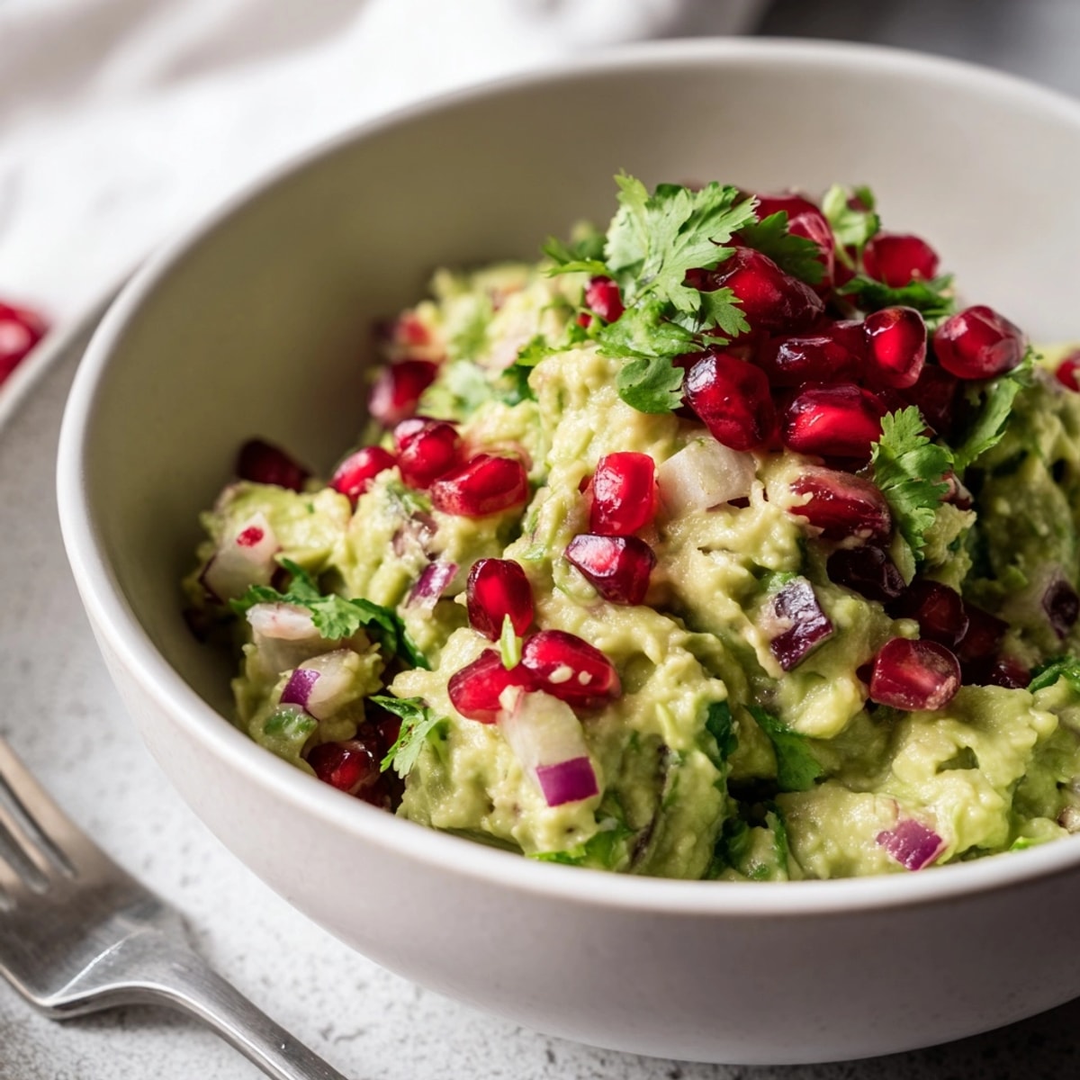 Creamy Pomegranate Guacamole, flecked with red jewels, ready to dip with crispy chips.