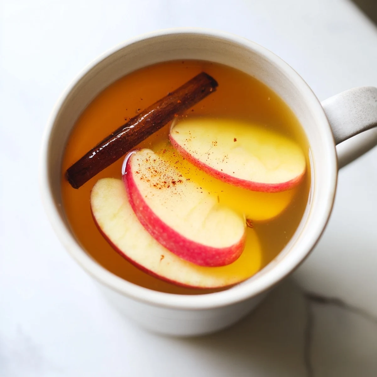 Close-up of a spiced warm apple cider, garnished with apple slices and a cinnamon stick.