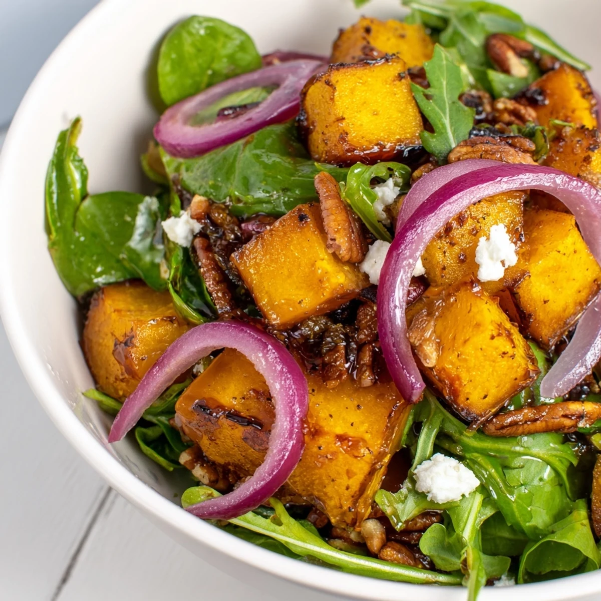Caramelized butternut squash salad with pecans and crumbled feta, served on a rustic wooden platter.
