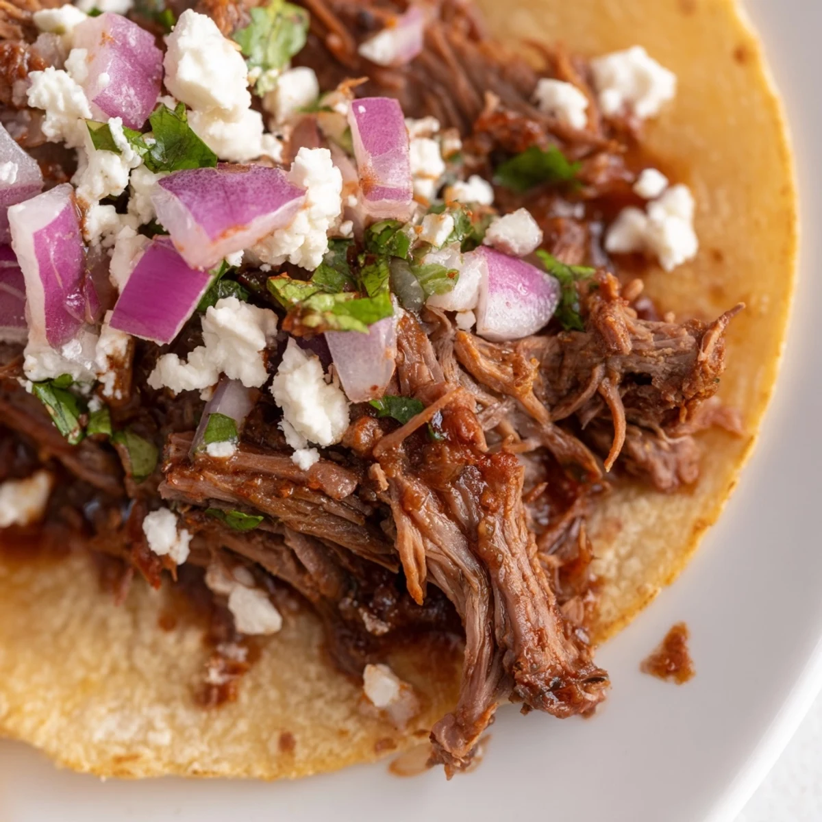 Slow-cooked shredded beef Barbacoa Tacos are piled high on warm corn tortillas with fresh cilantro and diced onions.