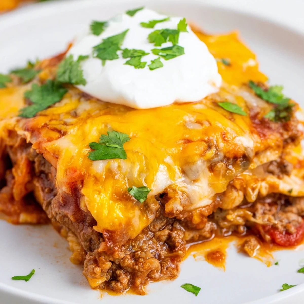 Steam rises from a freshly baked Beef Enchilada Casserole, served with a dollop of sour cream and sliced green onions.