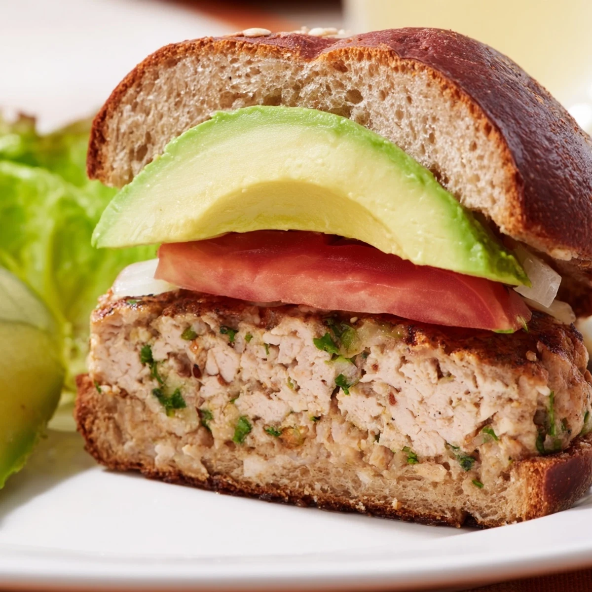 Freshly assembled Turkey Burger with Avocado features ripe avocado slices, red onion, and a smear of mayonnaise.