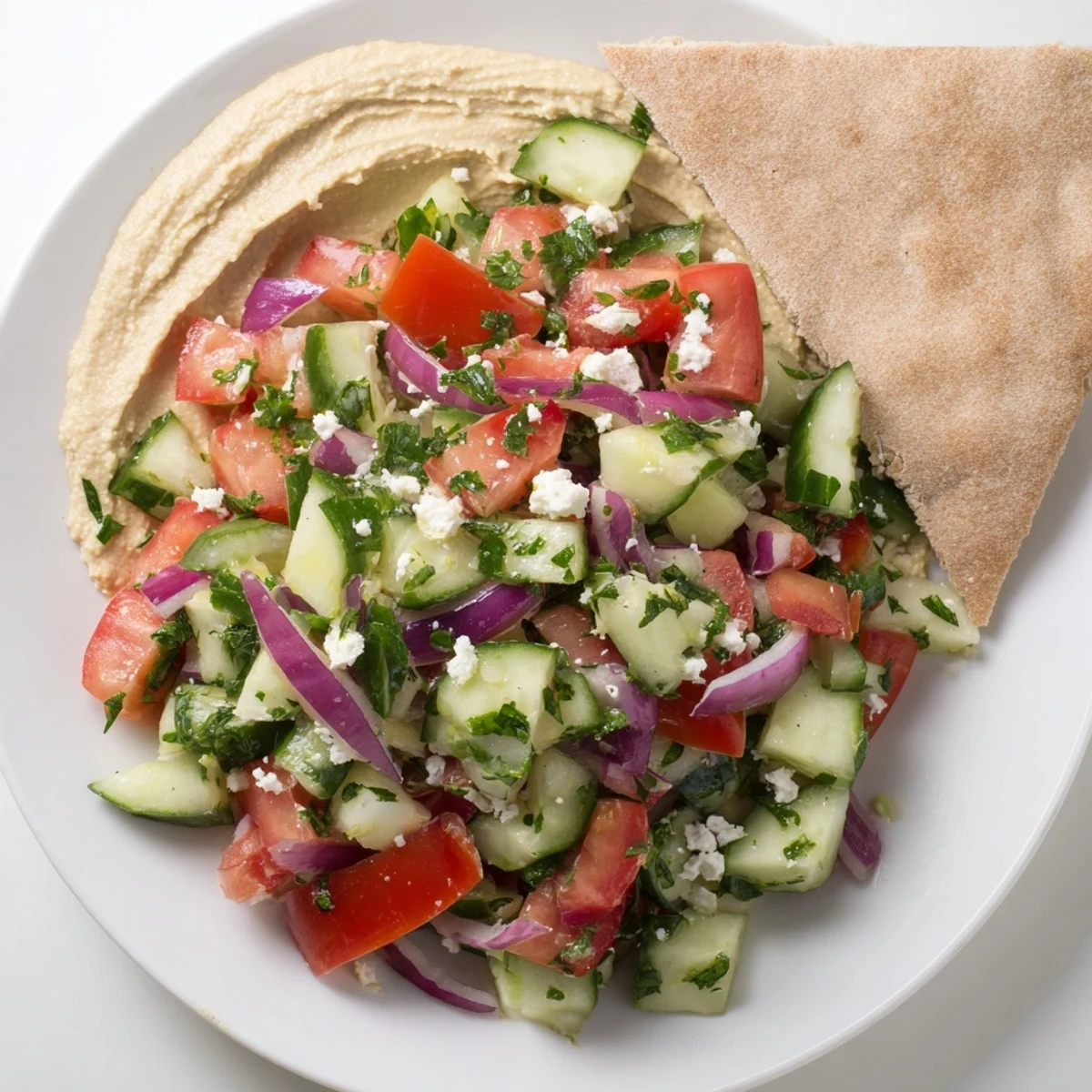 Bright lemon dressing and crumbled feta cheese top this vibrant Mediterranean Salad with Hummus and Pita Bread served on a rustic plate.