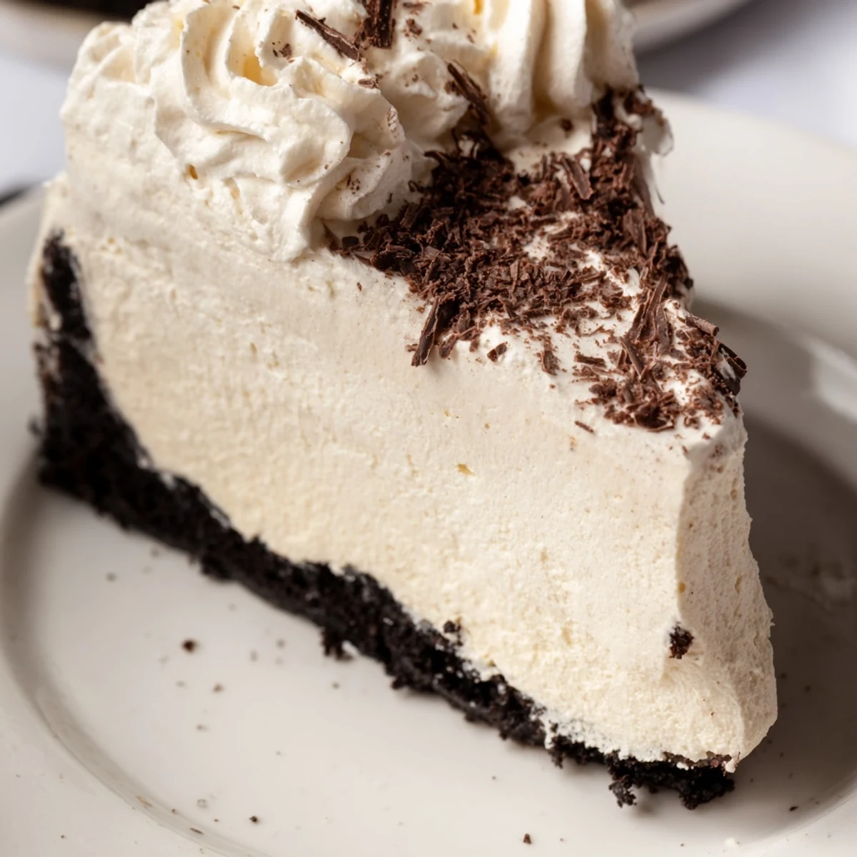 A creamy slice of Bailey Style Irish Cream Cheesecake with a chocolate cookie crust, topped with fluffy whipped cream.  