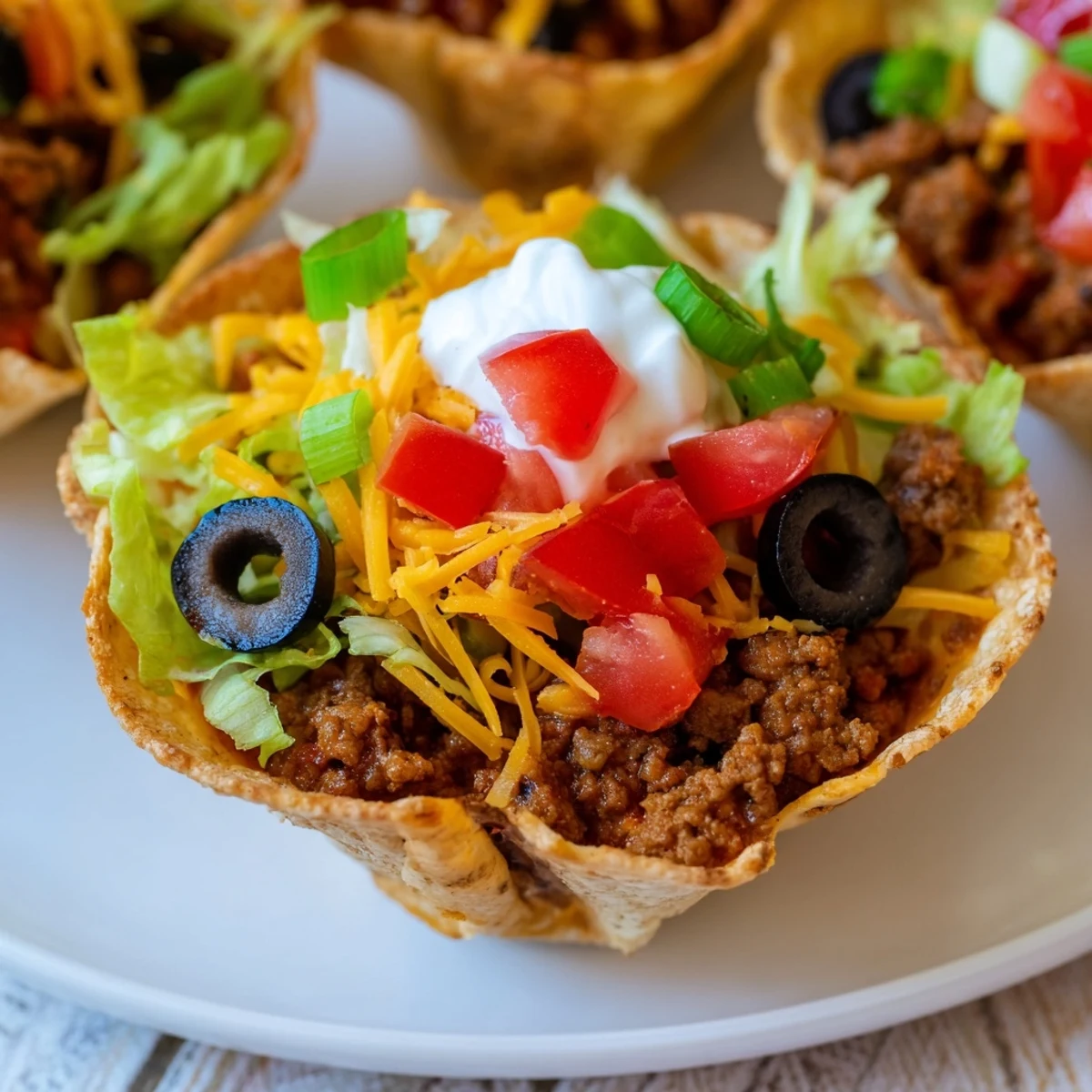 Golden-brown Touchdown Taco Cups with seasoned beef and melted cheese sit in a muffin tin, garnished with fresh toppings. 