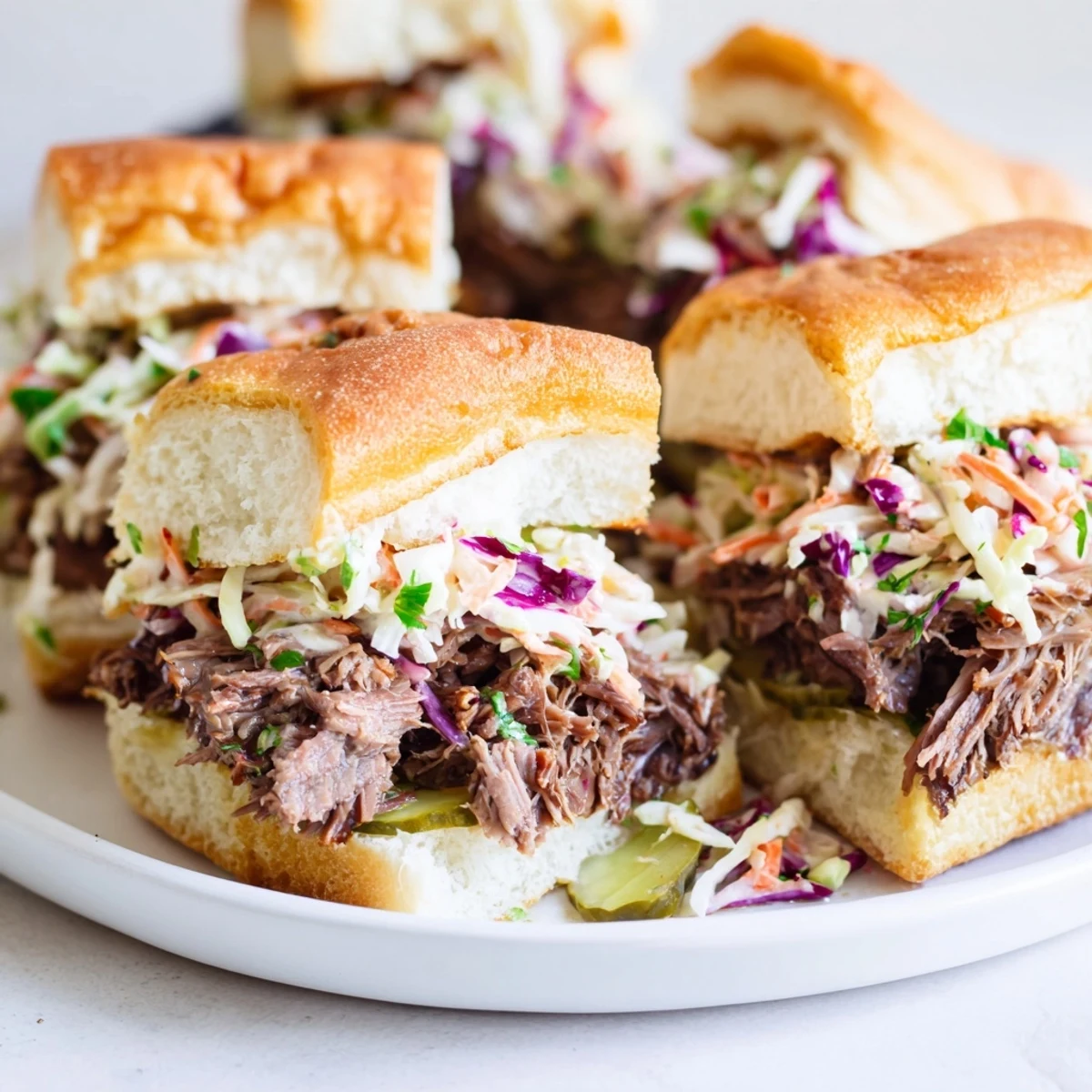 A close-up look at tender slow-cooked beef brisket sliders with crunchy coleslaw and pickle slices on soft buns.