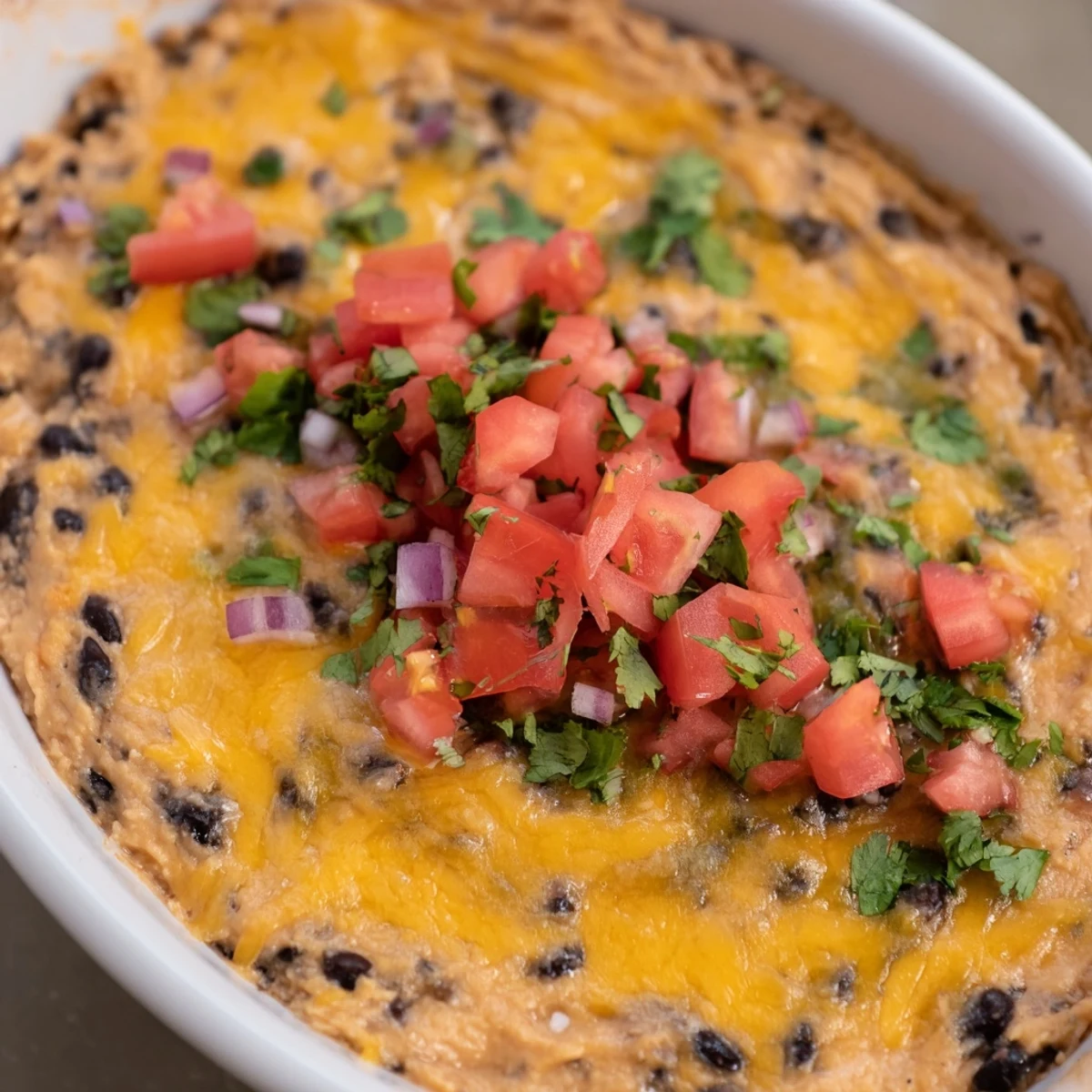 Warm Bean Dip with Cheddar Cheese alongside fresh veggie sticks and pita chips for dipping.