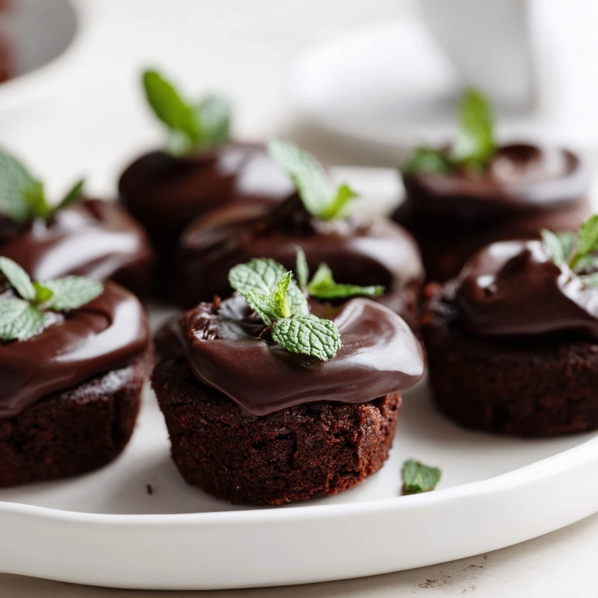 Glossy, fudgy Mint Brownie Bites topped with silky chocolate ganache and a fresh mint leaf garnish.  