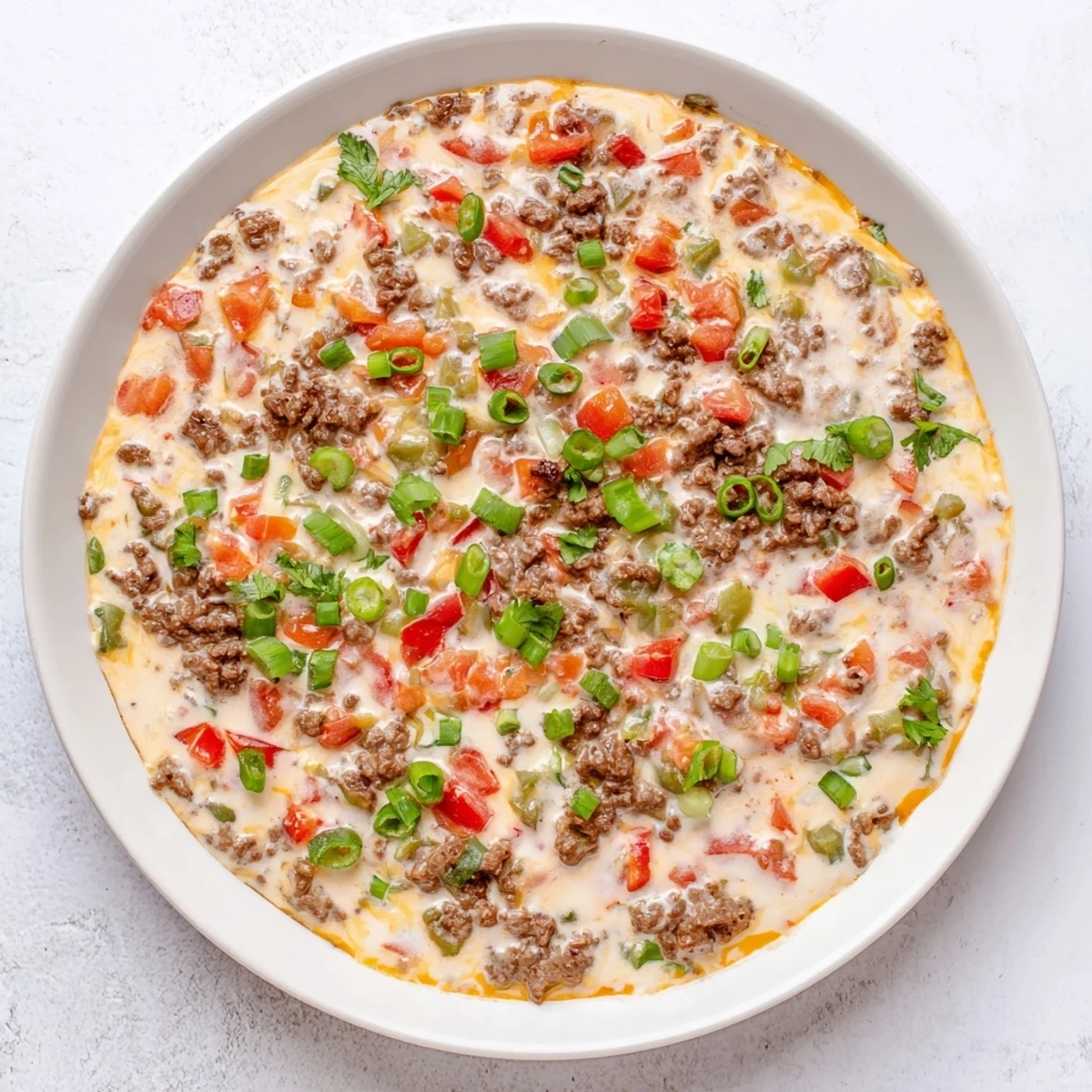 Close-up of warm, creamy Queso Dip with Ground Beef and Peppers, garnished with fresh cilantro and served with tortilla chips.