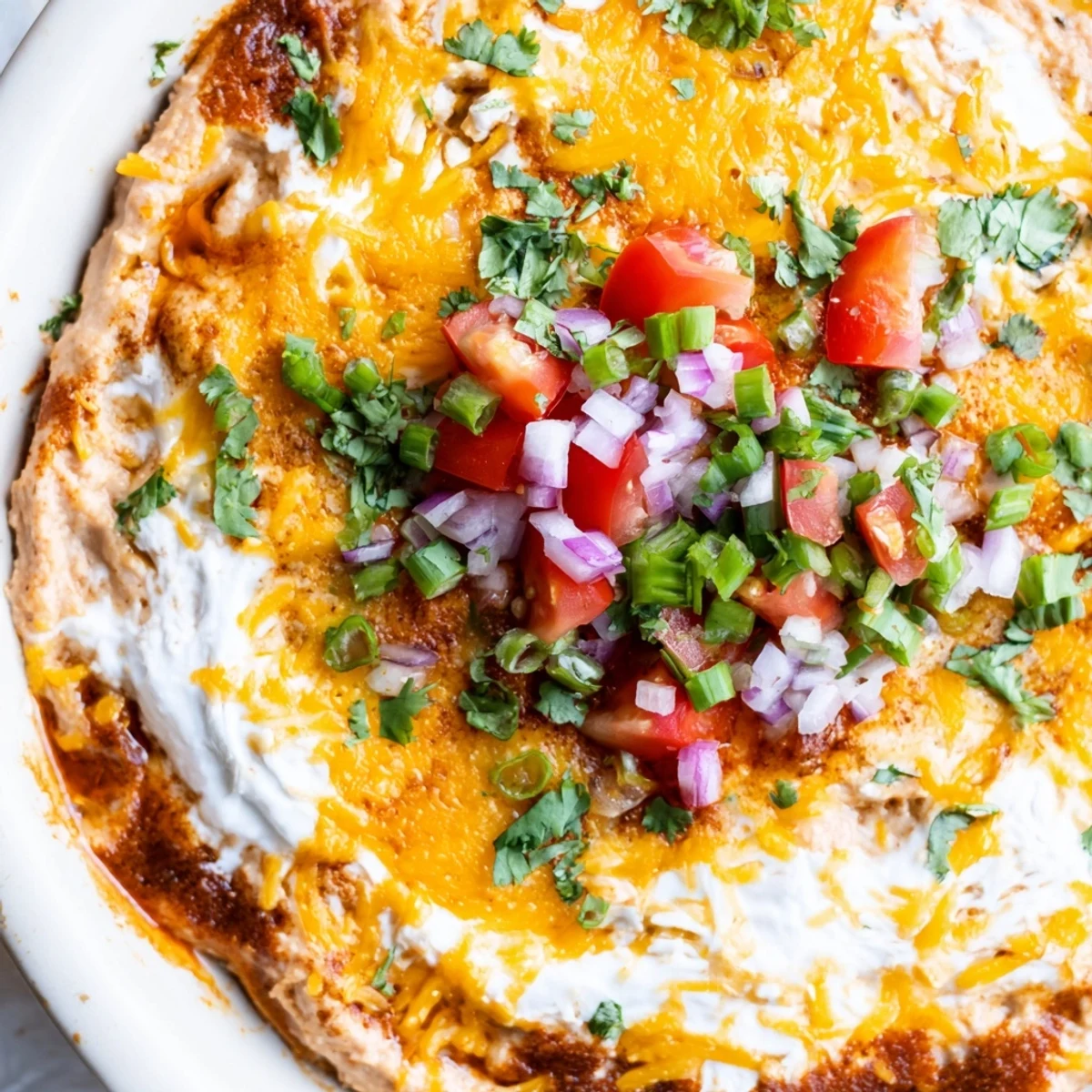 A close-up of hot, bubbly Bean Dip with Cheddar Cheese, garnished with fresh cilantro and diced tomatoes.