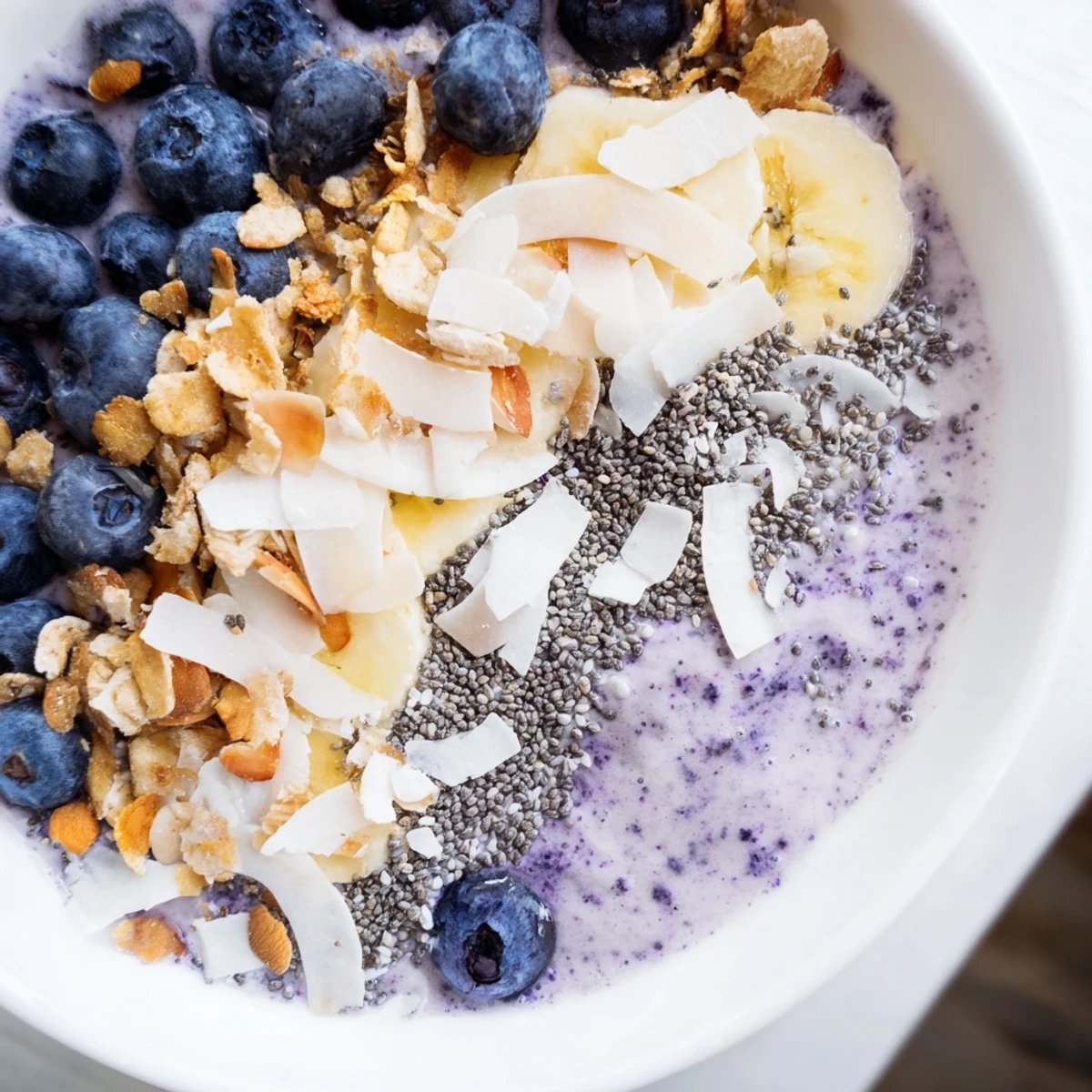 Close-up of a creamy Lemon Blueberry Smoothie Bowl with coconut flakes, chia seeds, and sliced almonds for texture.