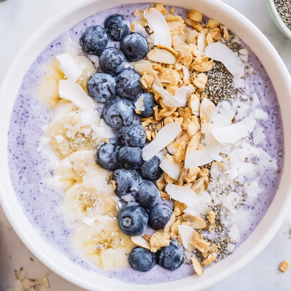 Brightly colored Lemon Blueberry Smoothie Bowl in a white bowl, garnished with fresh fruit and granola for a healthy start.