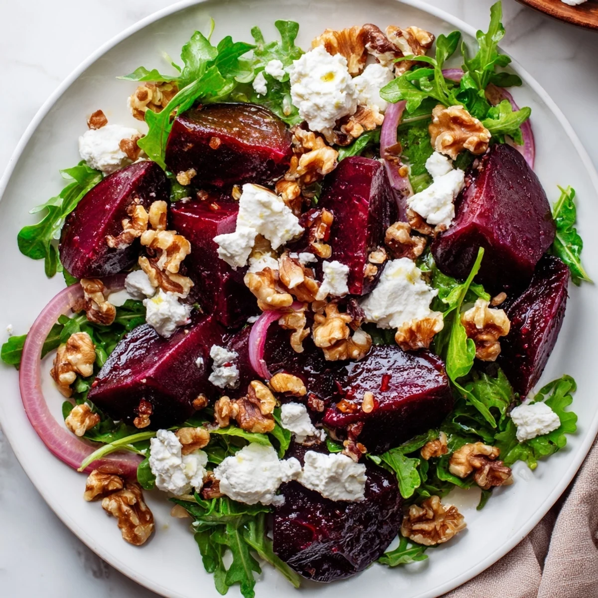Roasted beet salad with goat cheese presents glossy beet wedges, tangy cheese, and toasted walnuts beside a zesty vinaigrette on a dinner plate.