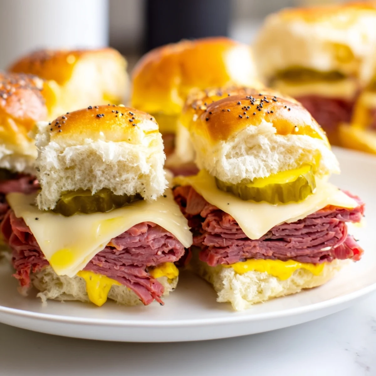 Corned beef sliders sit on a white plate with yellow mustard and crunchy dill pickles nearby.