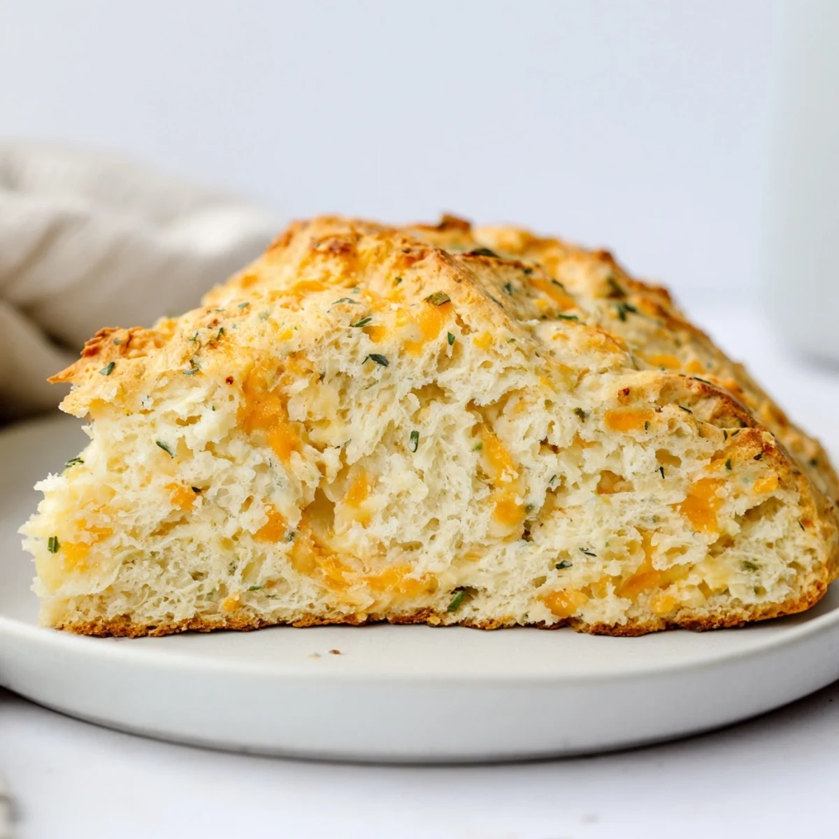 Freshly baked Savory Herbed Cheddar Irish Soda Bread sliced on a wooden board, next to a steaming bowl of soup.