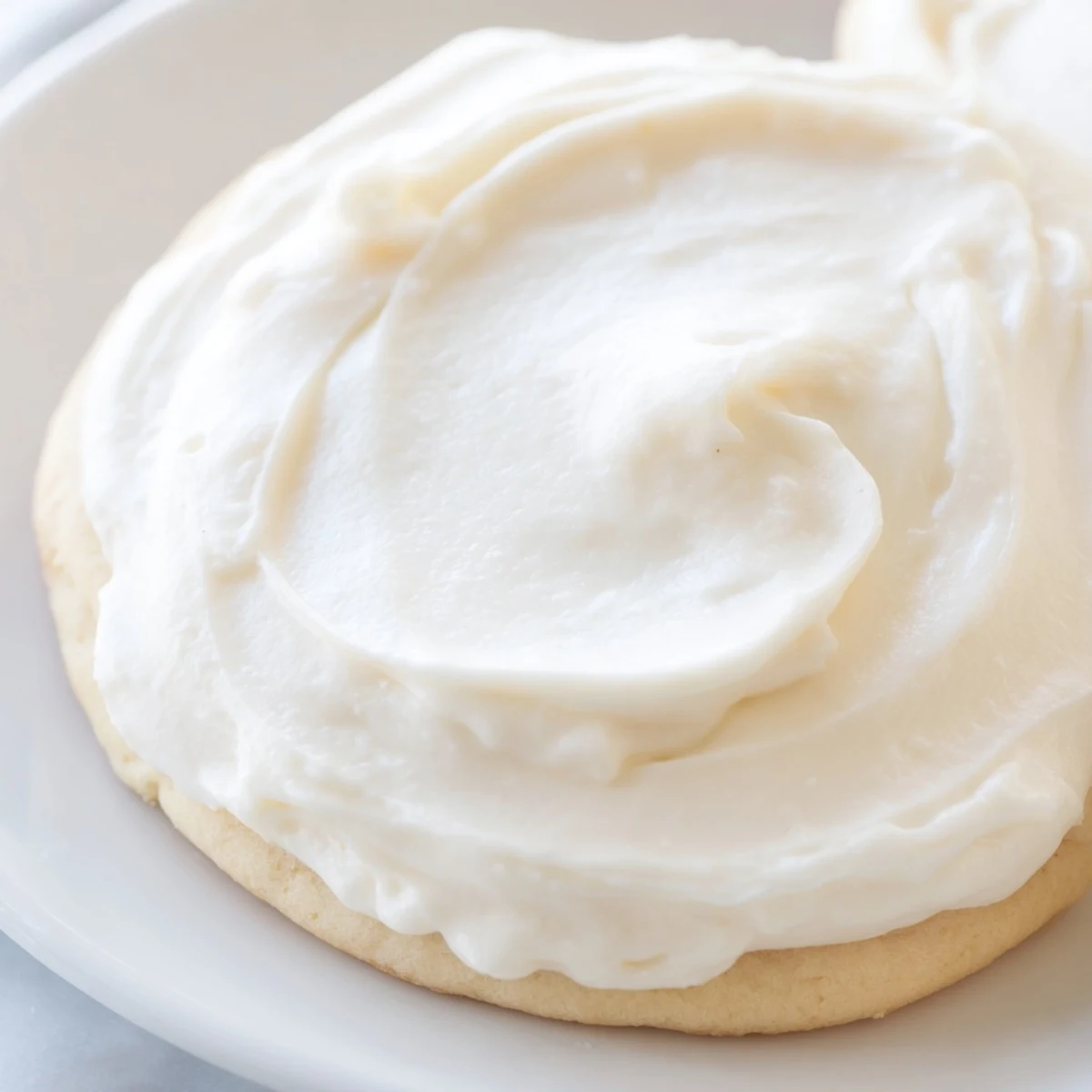 Easy Sugar Cookie Frosting in pastel colors beside decorated sugar cookies on a rustic wooden table.