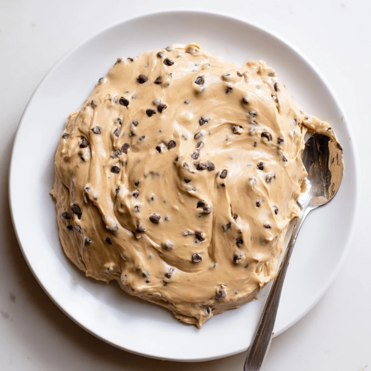 Creamy cookie dough frosting swirled with mini chocolate chips, perfect for generously topping vanilla cupcakes in a cozy kitchen.