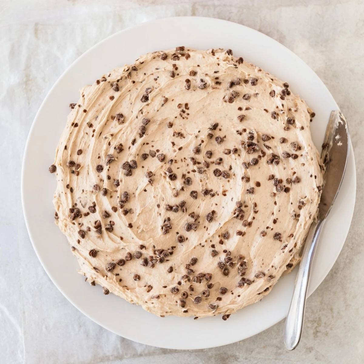 This easy cookie dough frosting shows a bowl of spreadable sweet goodness ready to frost a freshly baked chocolate cake.