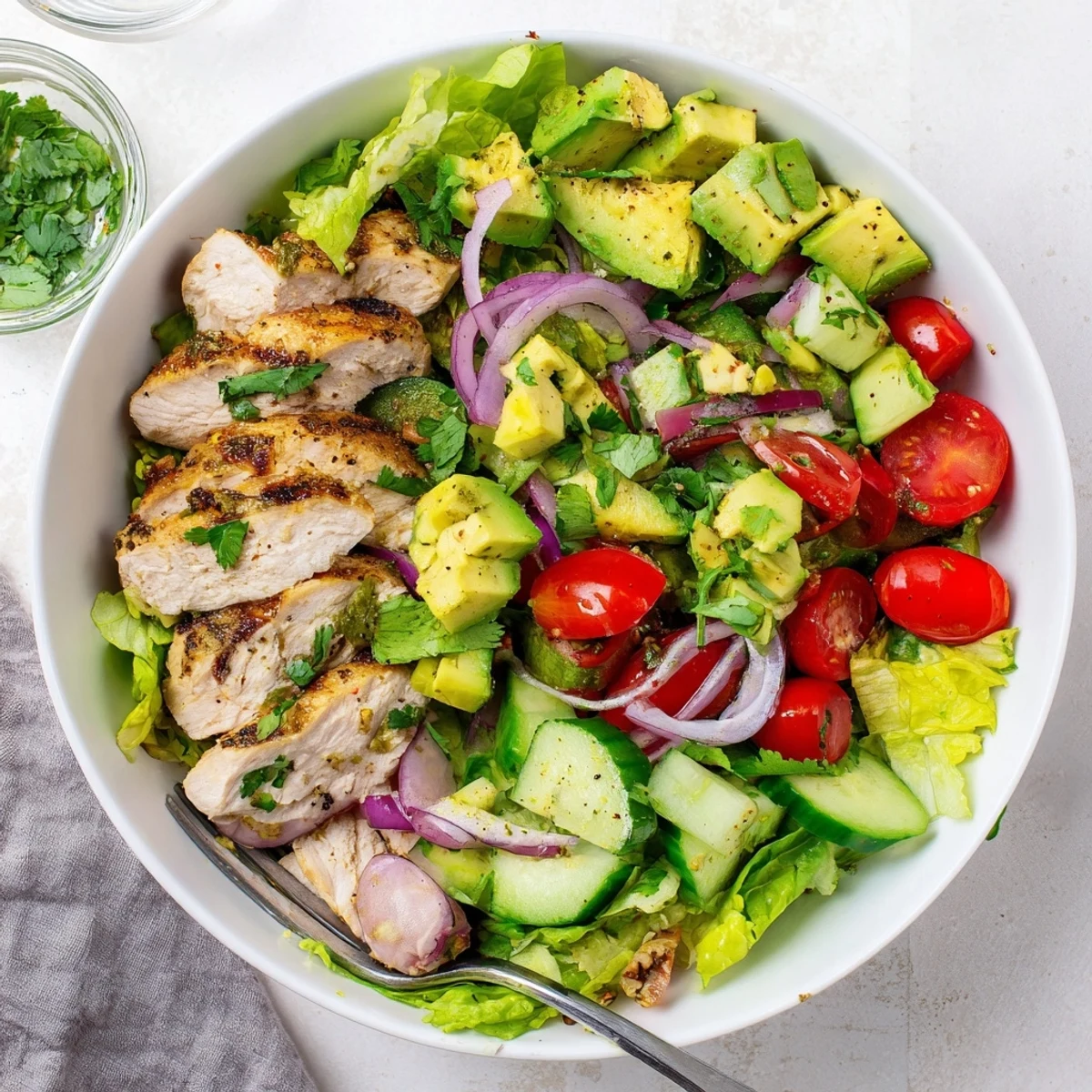 A vibrant bowl of Avocado Chicken Salad with diced chicken, creamy avocado chunks, and fresh cherry tomatoes on mixed greens.