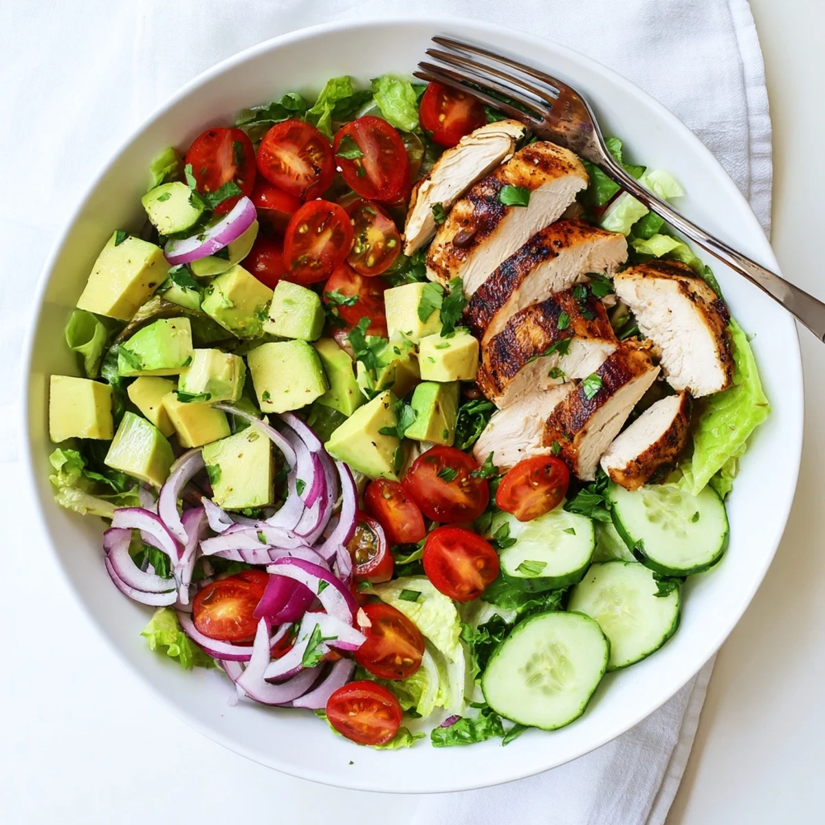 Serving suggestion for Avocado Chicken Salad over crisp lettuce, featuring juicy chicken and creamy avocado cubes beside red onion slices.