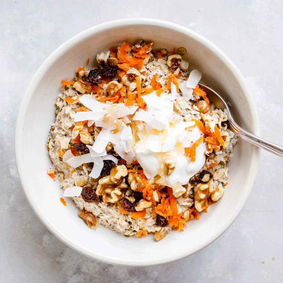 Healthy carrot cake overnight oats mixed with chia seeds, raisins, and warm spices, served chilled in a clear glass jar.