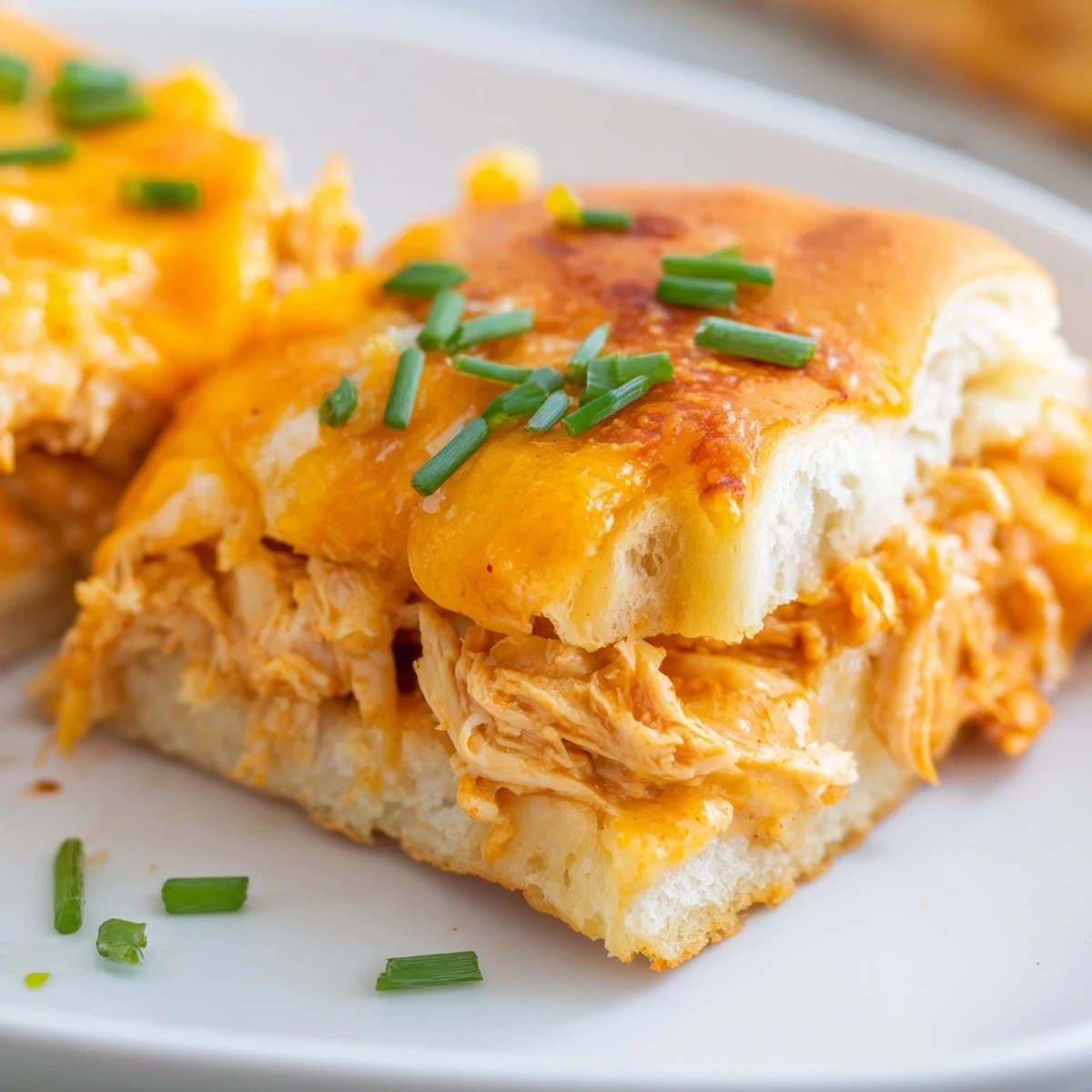 Spicy buffalo chicken dip filling oozing from sliders, topped with fresh chives and served on a platter.