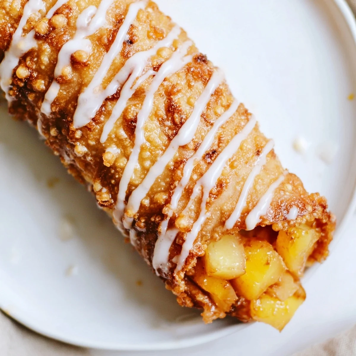 Crispy golden Peach Cobbler Egg Rolls drizzled with vanilla glaze on a rustic plate with fresh peach slices.