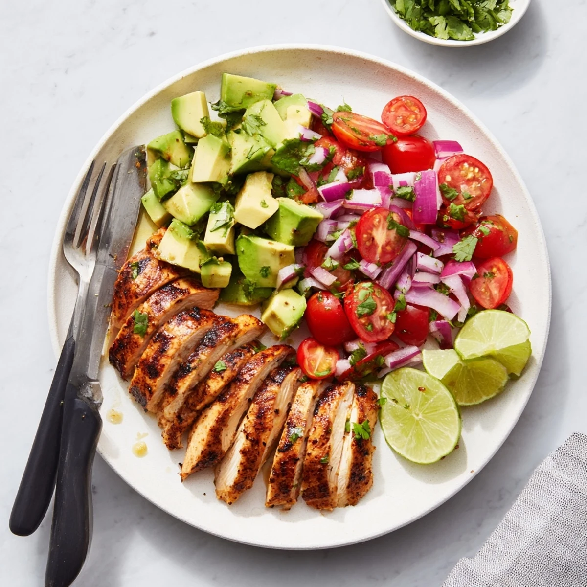Sliced spiced chicken breast arranged over colorful avocado salad garnished with fresh cilantro leaves