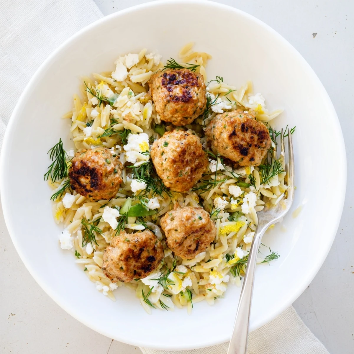 Juicy Mediterranean herb seasoned meatballs atop tender orzo pasta tossed with zesty lemon and parsley