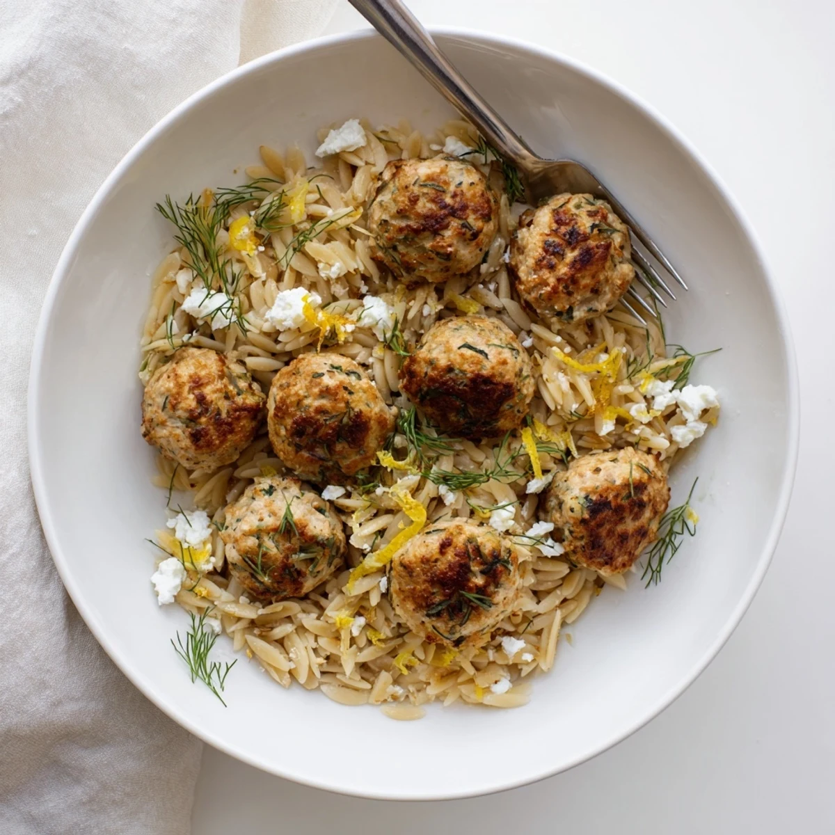 Golden chicken meatballs with fragrant orzo featuring citrus, garlic, and chopped fresh herbs in a bowl