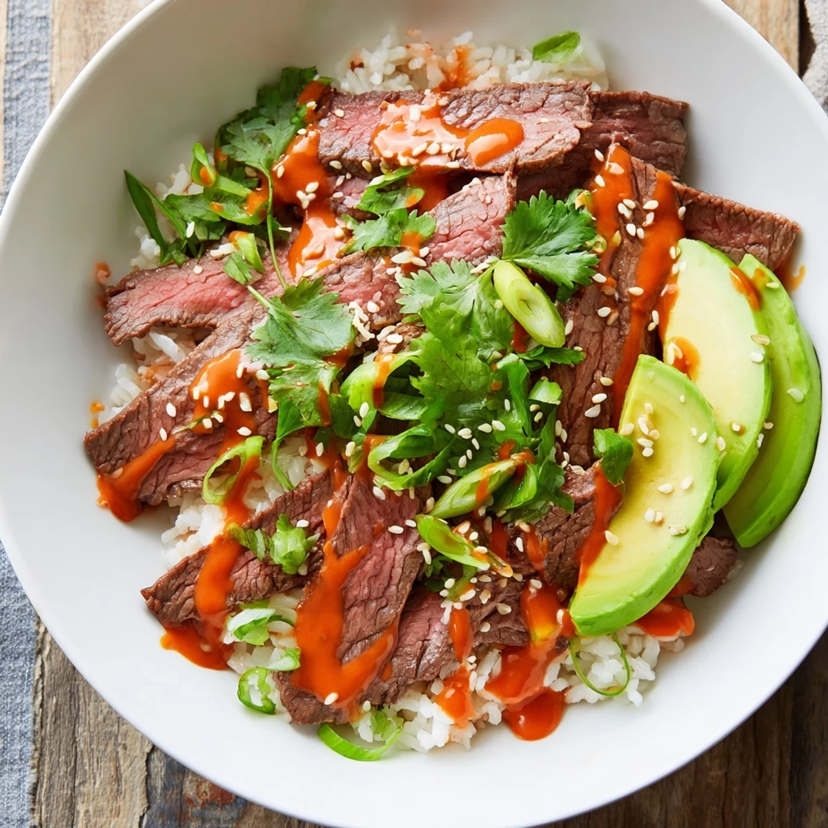 Flank steak bowl featuring juicy sliced beef over rice with fresh vegetables and spicy sriracha drizzle