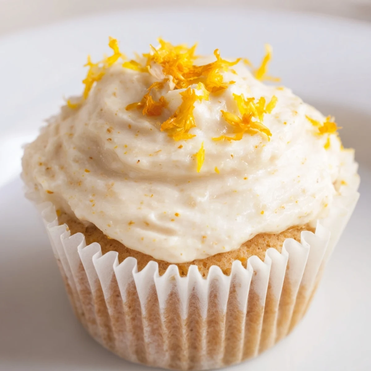 Golden orange blossom cupcakes topped with fluffy white citrus frosting and fresh orange zest garnish