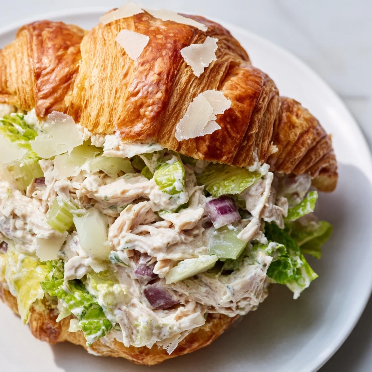 Buttery croissant sandwich loaded with Caesar chicken salad topped with fresh Parmesan shavings