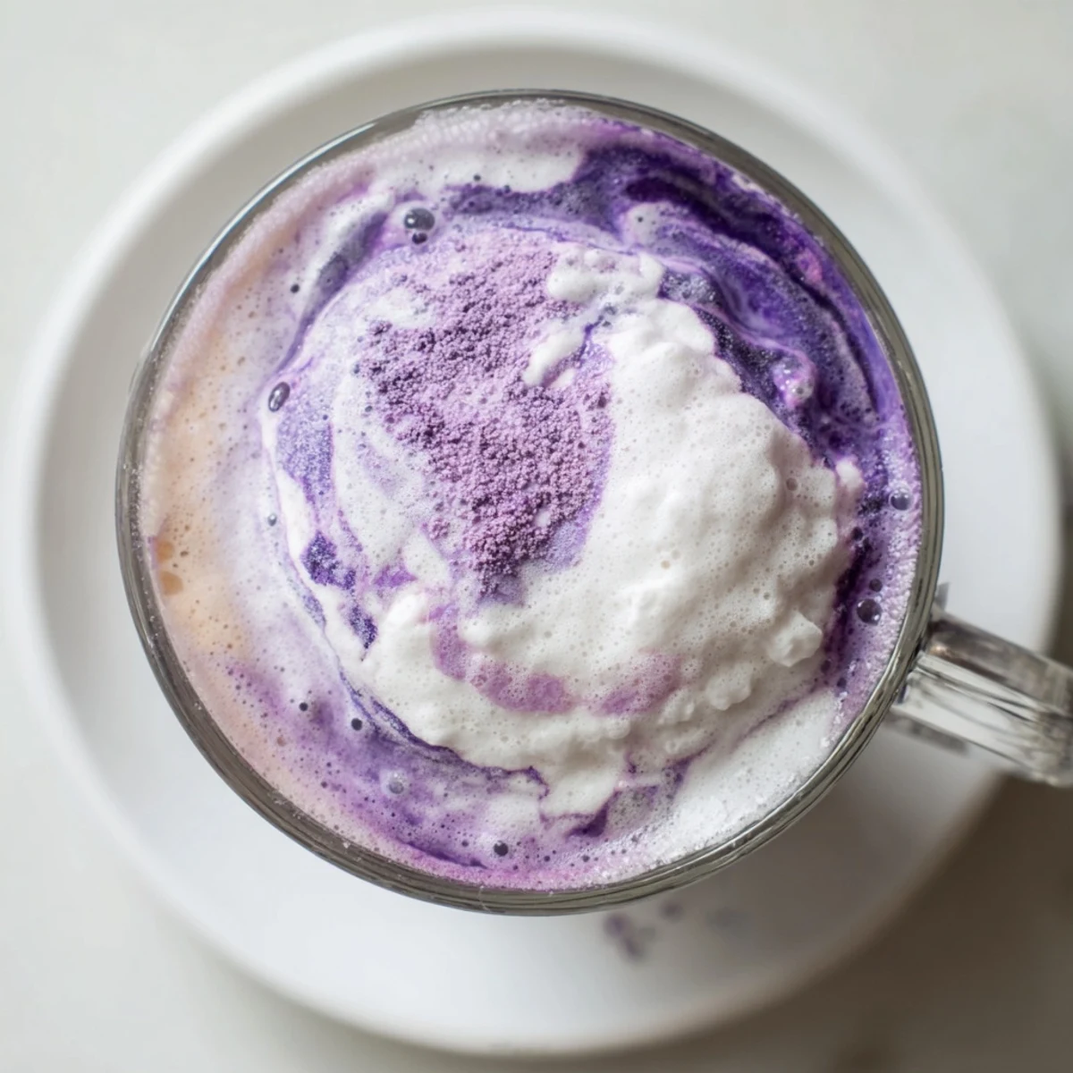 Vibrant purple ube latte topped with whipped cream and purple yam flakes in a glass