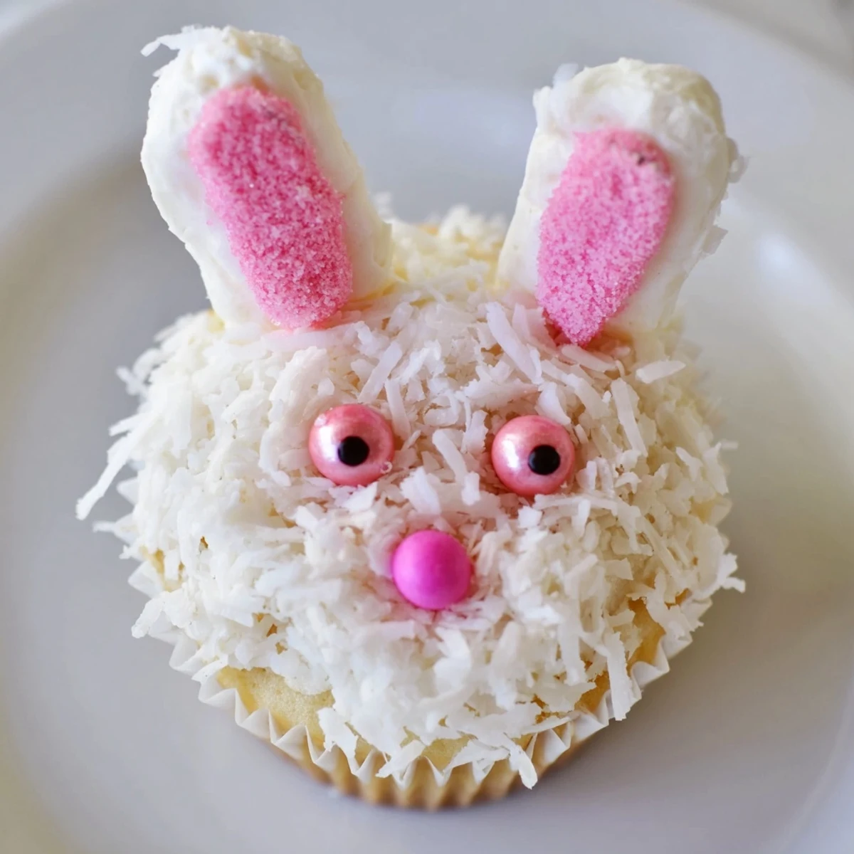 Adorable Easter bunny cupcakes featuring white coconut fur, pink sanding sugar ears, and jelly bean noses on vanilla treats