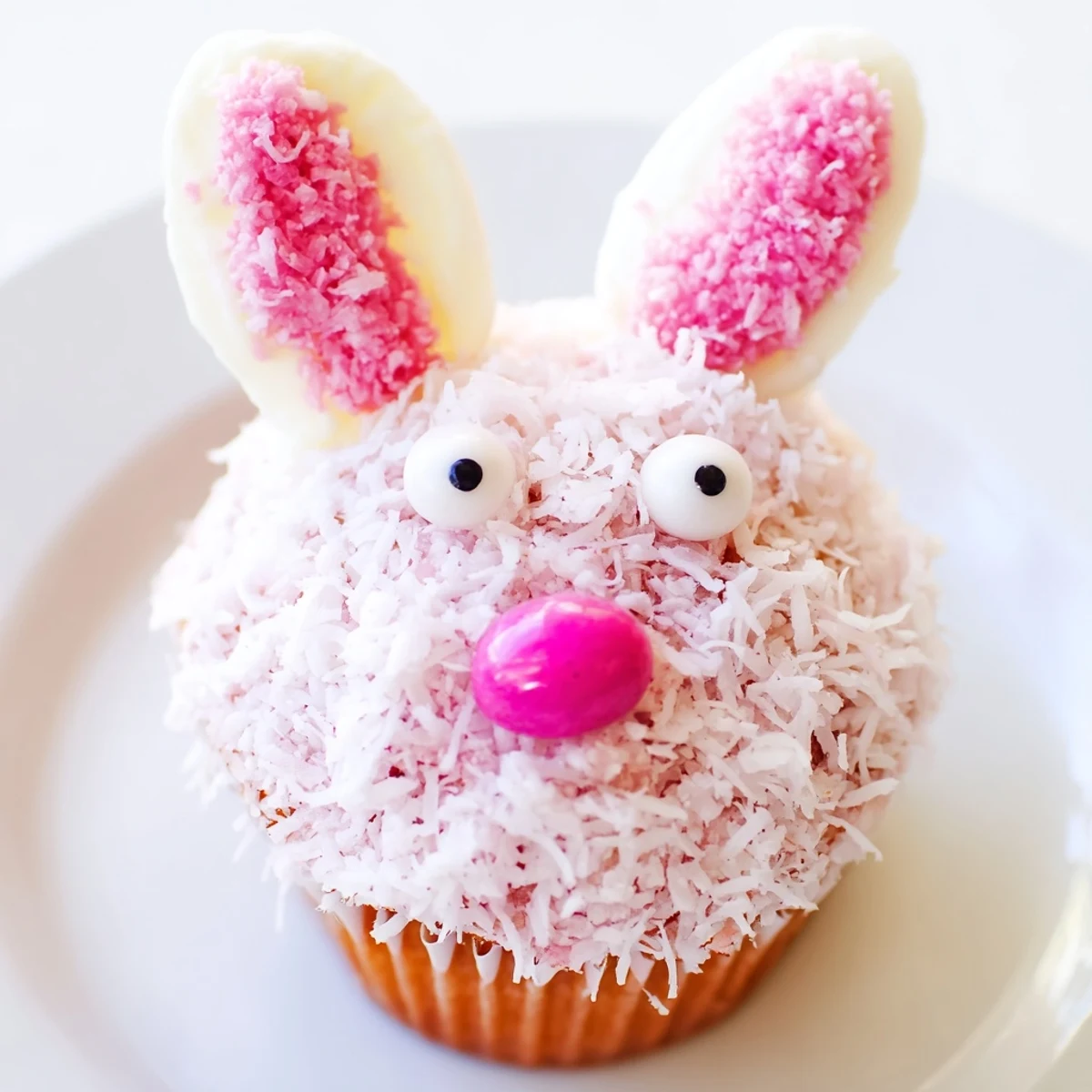 Decorated bunny cupcakes with fluffy coconut coating, marshmallow ears, candy eyes, and pink jelly bean noses for spring dessert