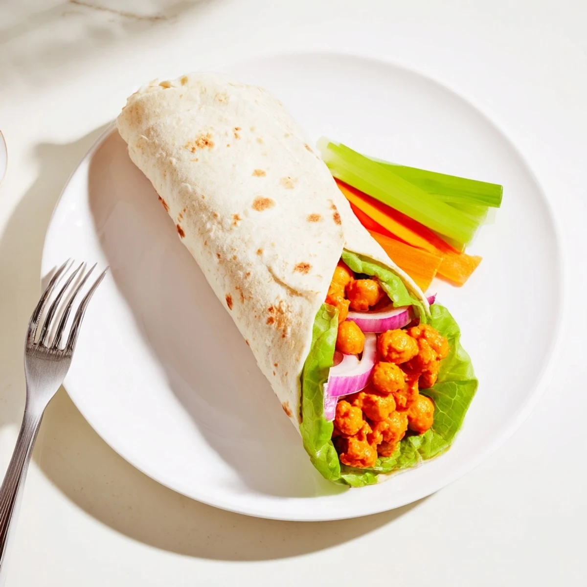 Spicy buffalo chickpea wrap with red onion, celery, and tangy sauce in tortilla