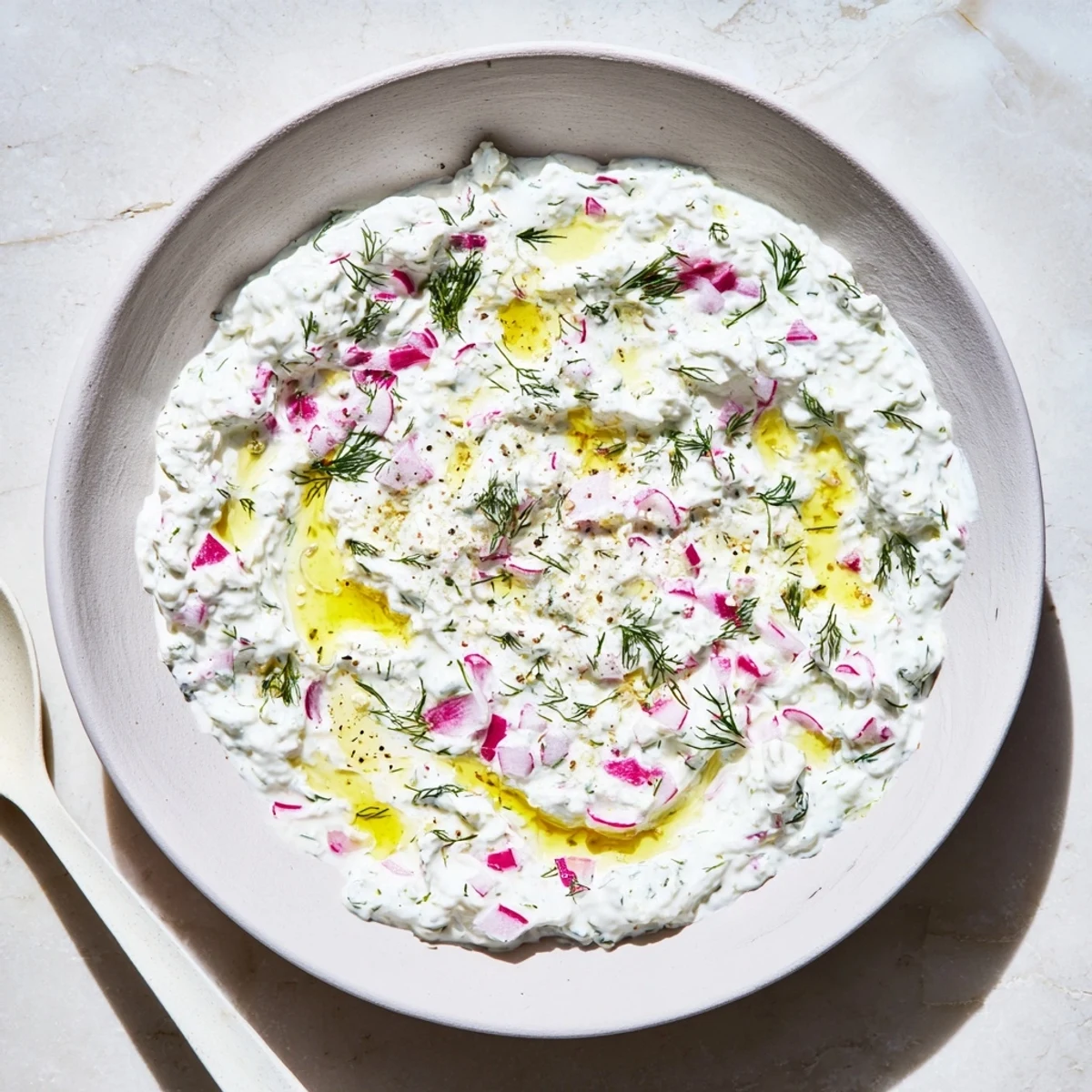 Creamy healthy radish tzatziki dip topped with fresh dill and served in a white bowl