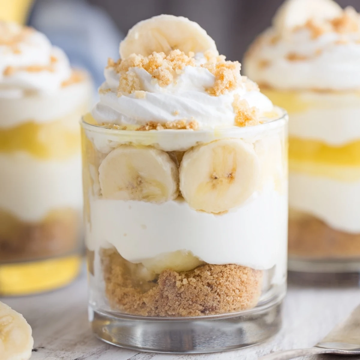 Individual no bake banana pudding cheesecake cups topped with golden wafer crumbs and sliced bananas