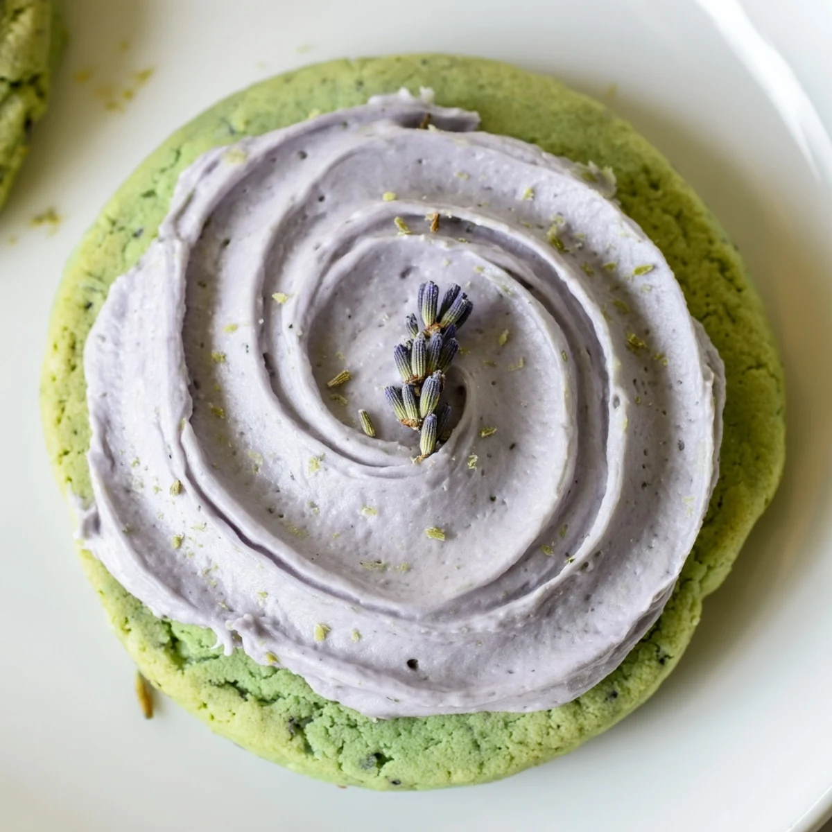 Soft green matcha sugar cookies with swirled lavender frosting on a rustic white plate