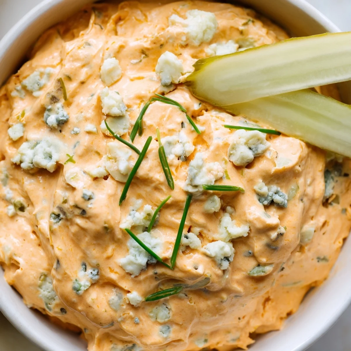 Creamy buffalo pickle dip in a serving bowl surrounded by crunchy chips and fresh veggie sticks