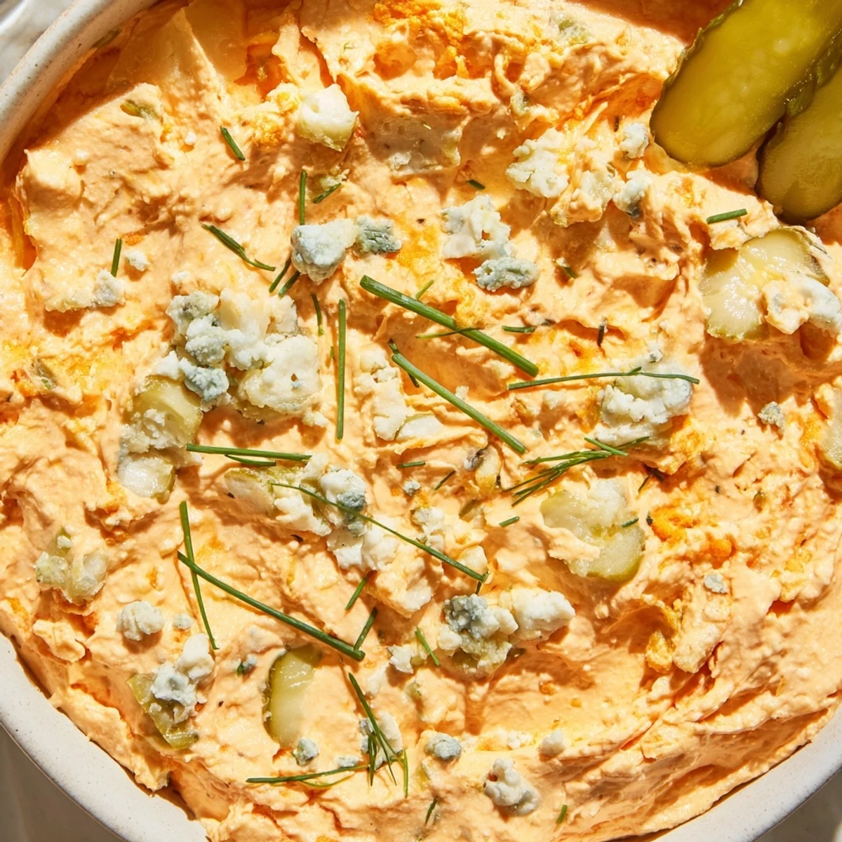 Tangy buffalo pickle dip topped with chopped chives and pickle slices on a rustic board