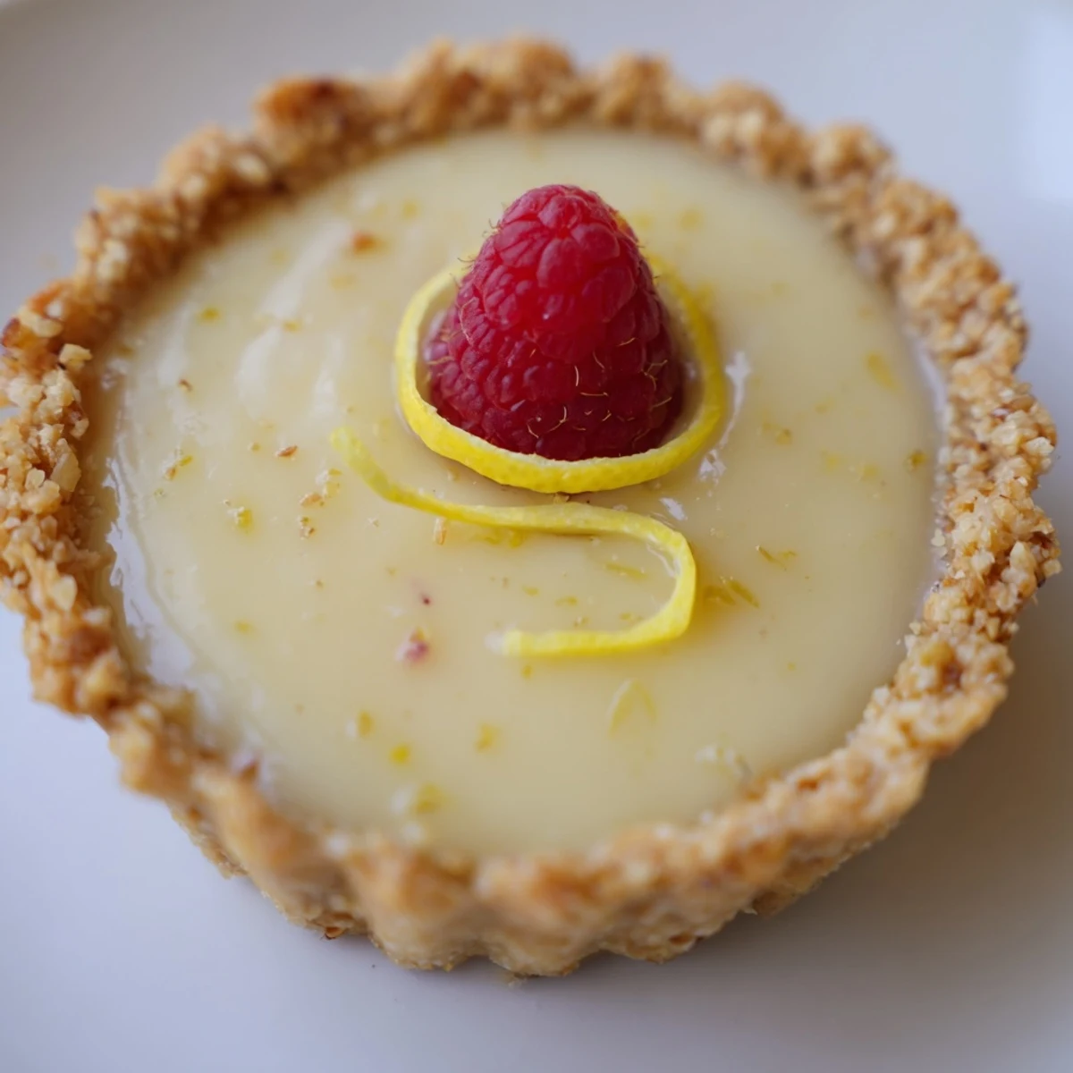 Golden mini vegan lemon tarts topped with fresh berries on a rustic white serving platter