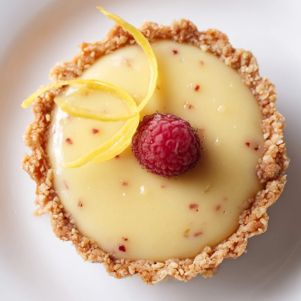 Creamy mini vegan lemon tarts in crisp almond crusts garnished with delicate lemon zest curls
