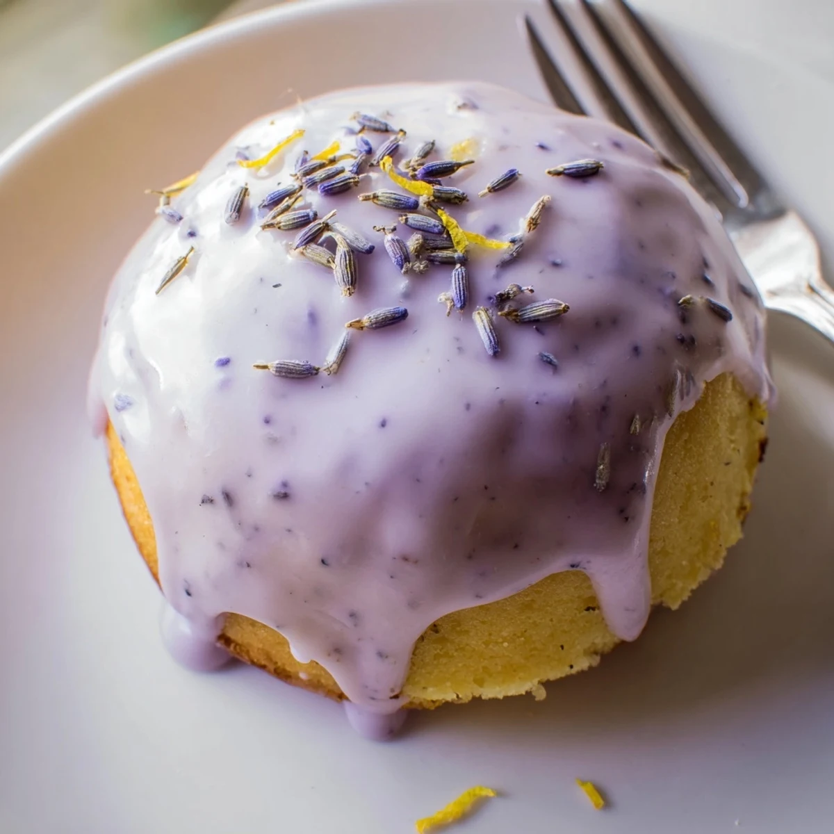 A batch of mini lemon cakes topped with smooth lavender glaze and scattered lemon zest