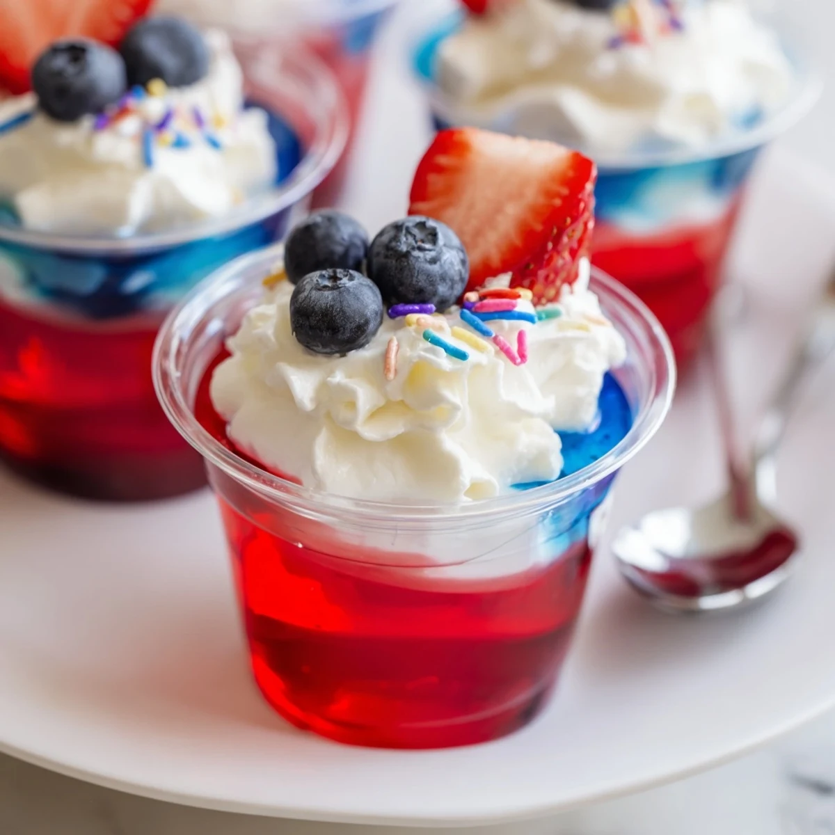 Red White And Blue Jello Cups layered in serving cups, topped with whipped cream.