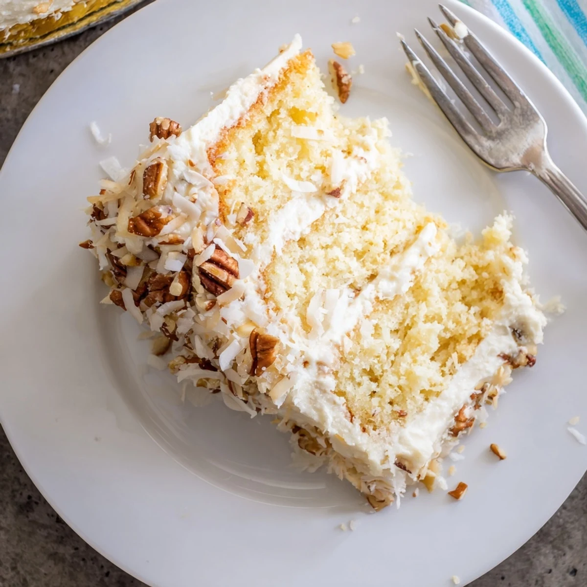 Slice of quick Italian cream cake showcasing fluffy coconut pecan layers beneath smooth cream cheese frosting
