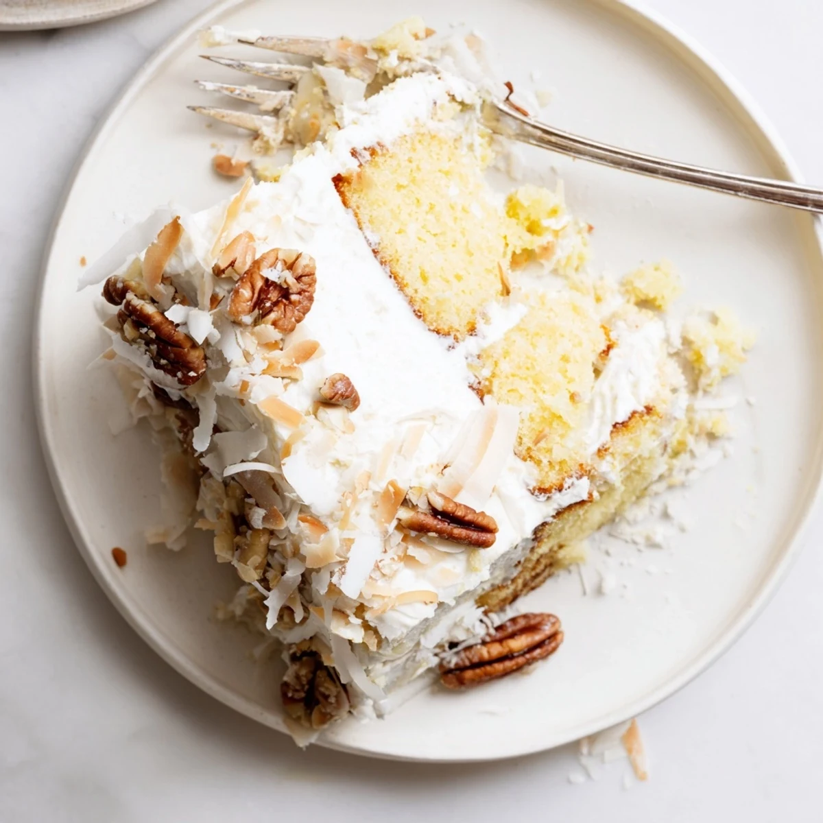 Moist Italian cream cake slice topped with creamy cream cheese frosting, toasted pecans, and shredded coconut