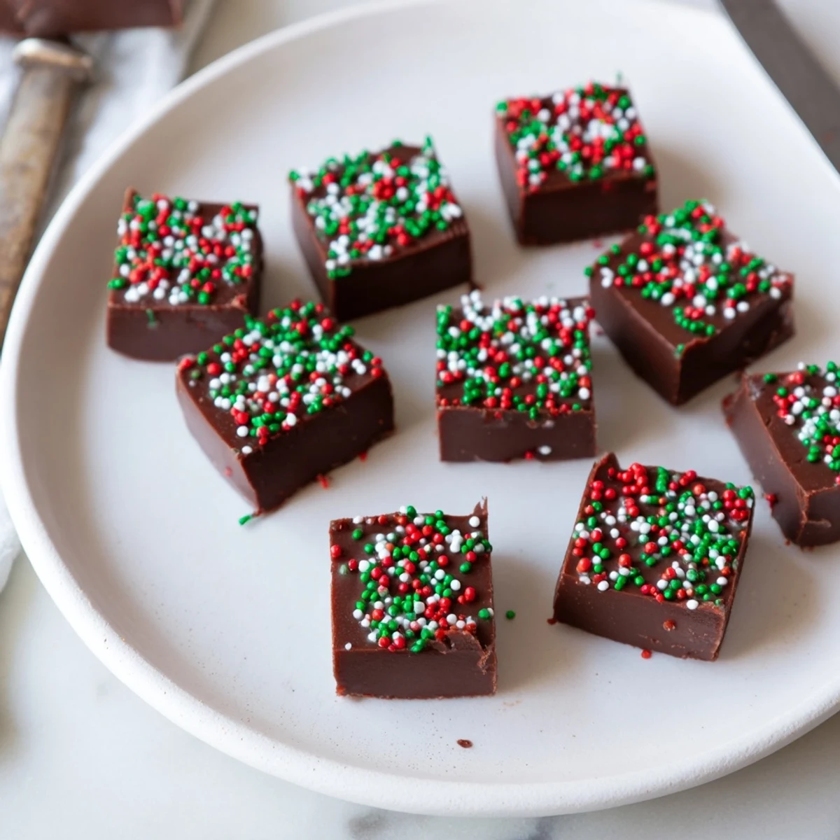 Creamy Christmas fudge with sprinkles cut into neat squares on a parchment-lined board