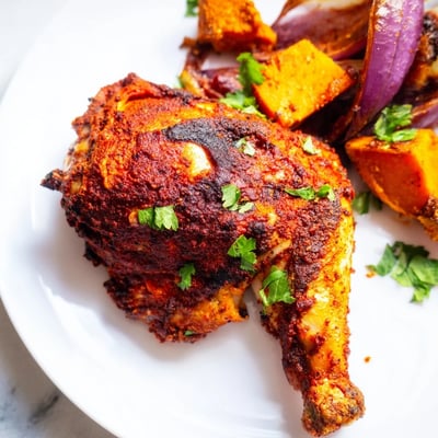 Spicy harissa-marinated chicken thighs paired with roasted sweet potato chunks and red onions on a sheet pan.